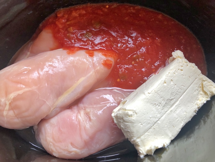 Ingredient needed to make creamy chicken slow cooker tacos including a block of cream cheese, a jar of salsa, and chicken breasts.