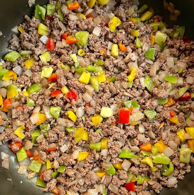 Cooked ground beef in a large skillet with chopped bell peppers and onion. 