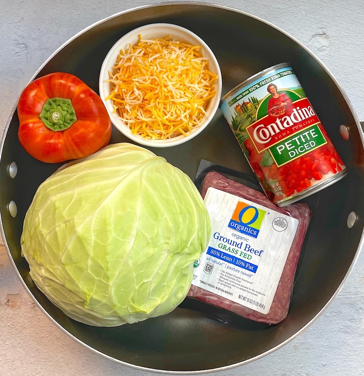 Large pot full of the ingredients needed to make a keto cabbage roll dinner skillet including a head of cabbage, ground beef, cheese, bell pepper, and a can of tomatoes. 